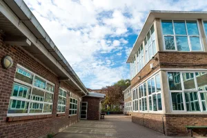 UK school exterior walls with lots of glass windows and built from brick, against the backdrop of a cloudy sky.